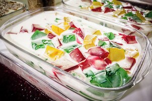 Una bandeja de postres con colores y texturas en capas, incluyendo elementos blancos, rojos, amarillos y verdes.