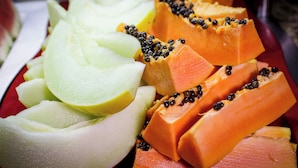 Variedad de frutas cortadas, incluyendo papaya y melón, sobre un plato rojo.