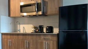 Uma cozinha moderna com armários de madeira, micro-ondas de aço inoxidável, geladeira preta e cafeteira.