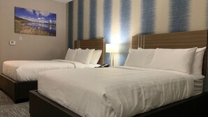 Quarto de hotel com duas camas, uma mesa de cabeceira, um abajur e um quadro com uma paisagem.