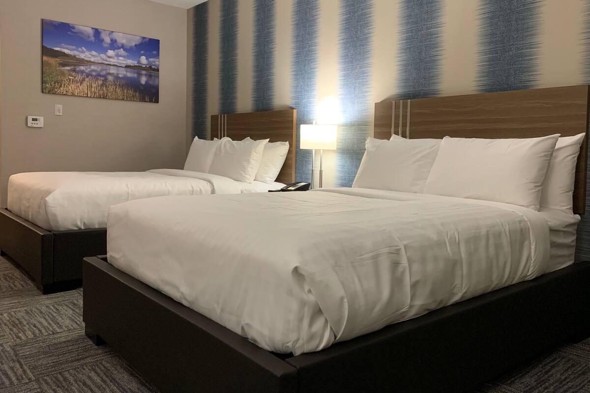 A hotel room with two beds, a nightstand, a lamp, and a painting of a landscape.