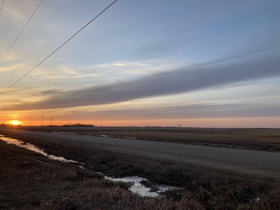 A rural landscape with a dirt road, fields, and a sunset.