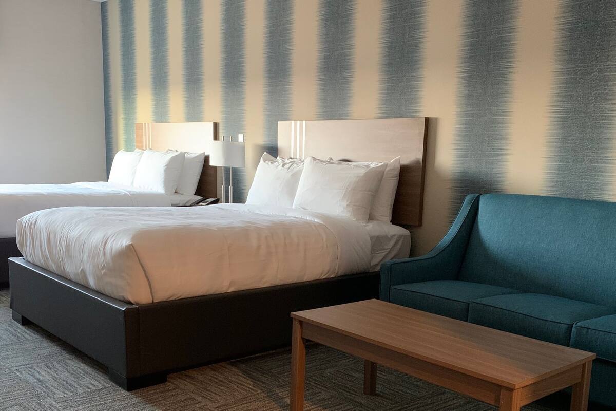A hotel room with two beds, a blue sofa, and a wooden table.