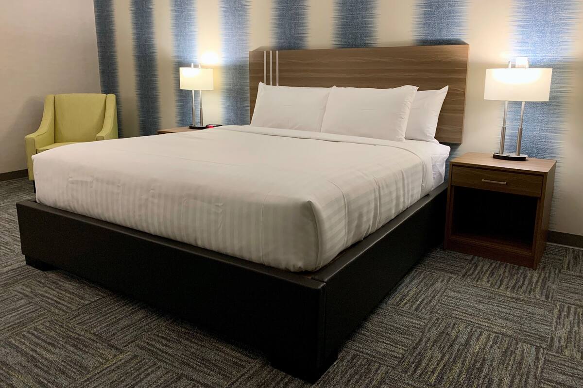 A hotel room with a large bed, two bedside tables with lamps, a chair, and a textured wall.