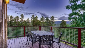 A wooden deck with a round table and chairs, surrounded by a metal fence. - Mountain View Retreat - Epic Views, Pool Table & Garage (Rollinsville)