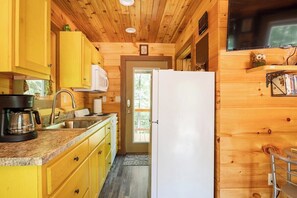 A compact kitchen with wooden walls, a white refrigerator, and a coffee maker on the counter. - Barn Owl Inn Treehouse - Private Hot Tub (Guild)