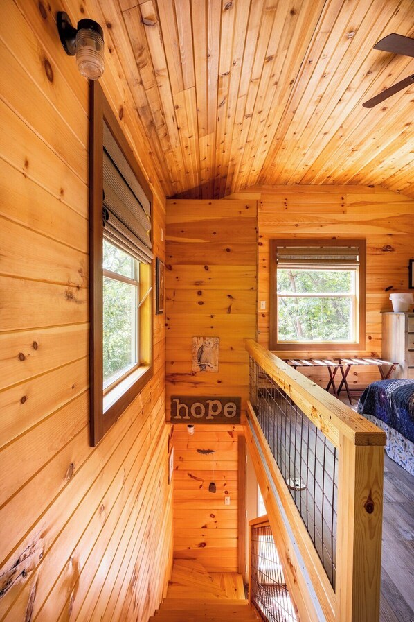 Interior de una cabaña de madera con una escalera que conduce a una zona de camas tipo altillo.