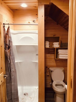 A wooden cabin bathroom with a shower, toilet, and shelves for towels. - Barn Owl Inn Treehouse - Private Hot Tub (Guild)
