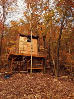 A wooden cabin with a balcony, surrounded by trees and autumn leaves. - Barn Owl Inn Treehouse - Private Hot Tub (Guild)