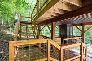 A wooden deck with a staircase leading to a covered area, surrounded by trees.