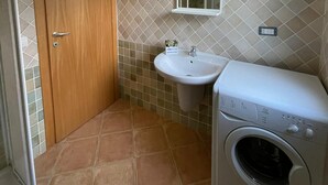Un baño pequeño con puerta de madera, un lavabo, un espejo y una lavadora.