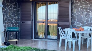 Un patio con un muro de piedra, una puerta corrediza de vidrio, una mesa con sillas y una pequeña mesa verde con una banca para pesas.