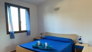 Un dormitorio con cama, dos mesitas de noche, ventana con cortinas e iluminación fijada a la pared.