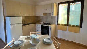 Una cocina compacta con una mesa de comedor lista para cuatro personas, un refrigerador, una estufa y una ventana con cortinas.