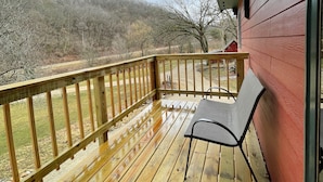 A wooden deck with a bench, overlooking a forested area. - River Valley Cabin (Lansing)
