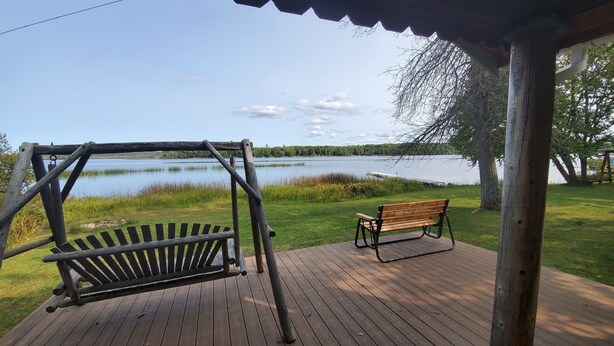 Eine Holzterrasse mit Schaukel und Bank mit Blick auf einen See.