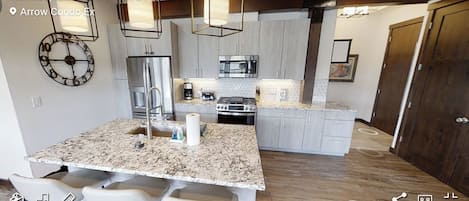 Una cocina moderna con encimeras de granito, electrodomésticos de acero inoxidable e iluminación colgante.