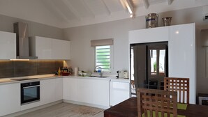 Une cuisine moderne avec des meubles blancs, un four encastré et une table à manger en bois, accompagnée de chaises.