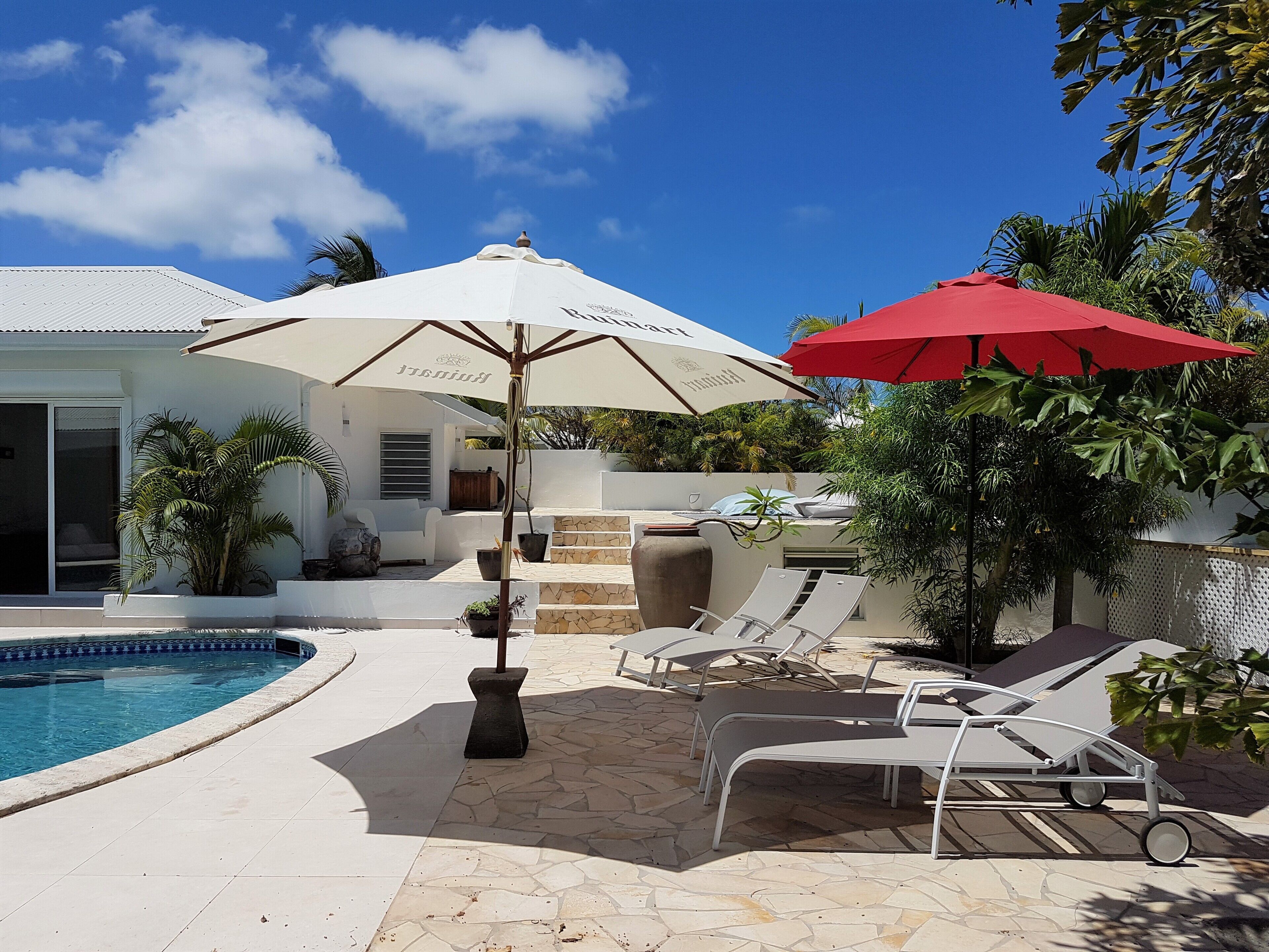 A poolside area with lounge chairs, a red umbrella, and a white umbrella.