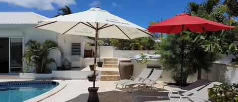 A poolside area with lounge chairs, a red umbrella, and a white umbrella.