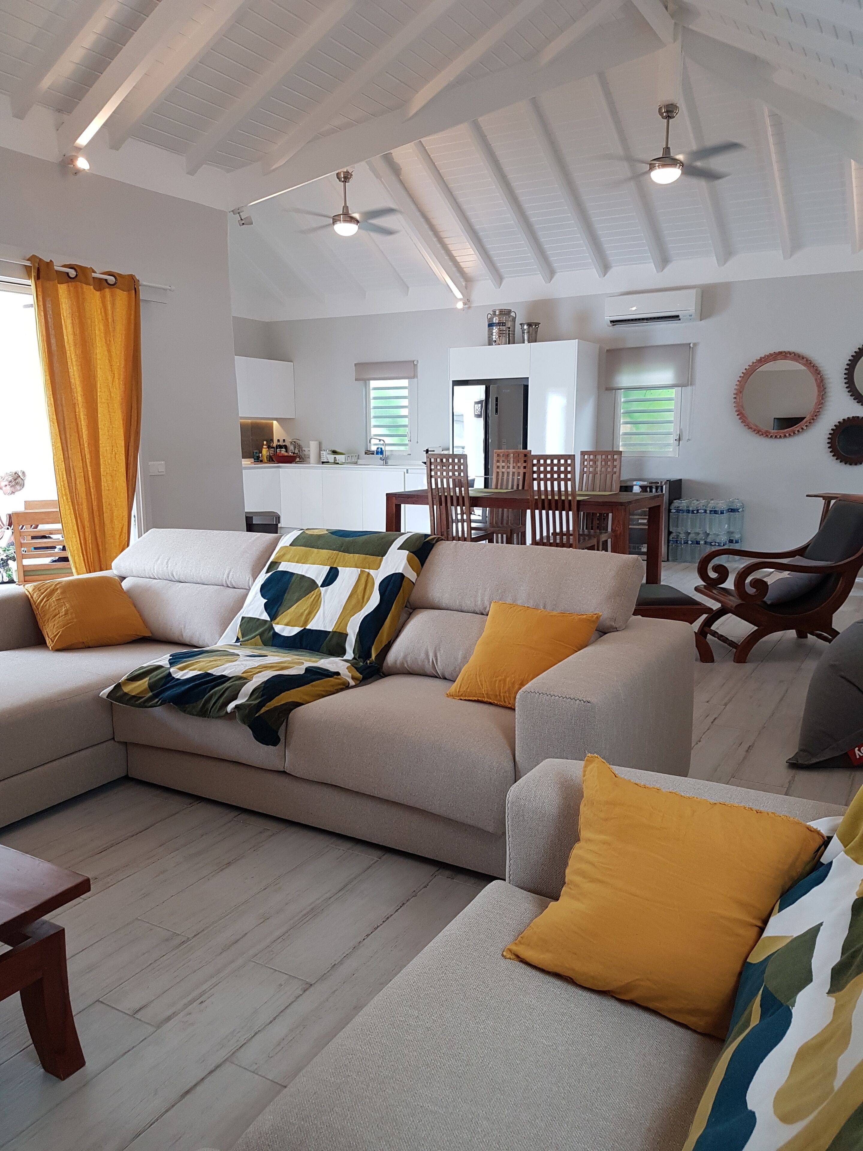 Una sala moderna con un sofá seccional color beige, sillas de madera y una mesa de comedor.