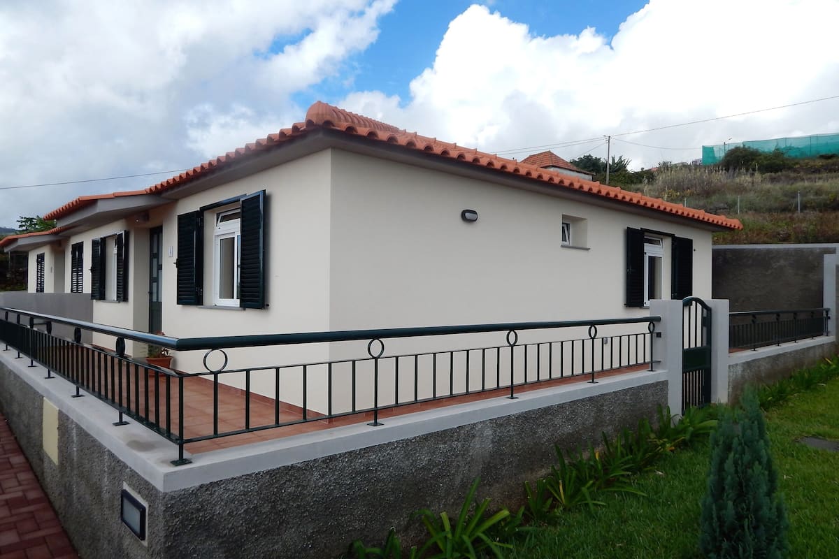 A two-story house with a tiled roof, white walls, and black shutters.