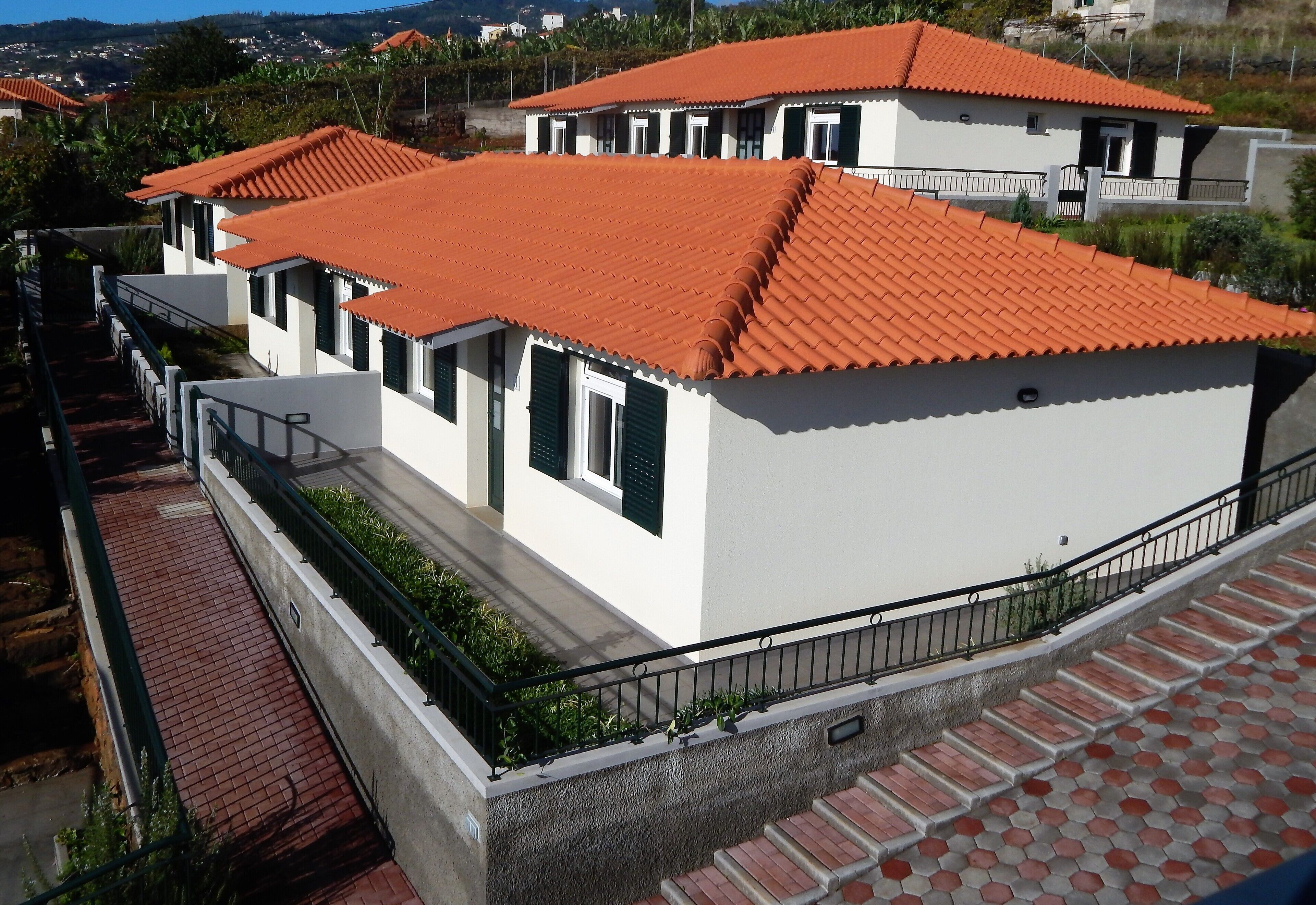 A residential building with a red-tiled roof, white walls, and a balcony with a black railing.