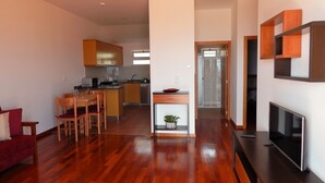 Eine moderne Wohnung mit Holzboden, einem Essbereich mit Tisch und Stühlen, einer Küche mit Holzschränken, einem Wohnzimmer mit Fernseher und einem Flur zu einer Tür.