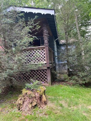 A wooden cabin with a balcony, surrounded by dense trees and a moss-covered stump.