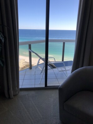 Une pièce dotée d’une grande fenêtre donnant sur une plage et l’océan. On y aperçoit une chaise et une petite table au premier plan.