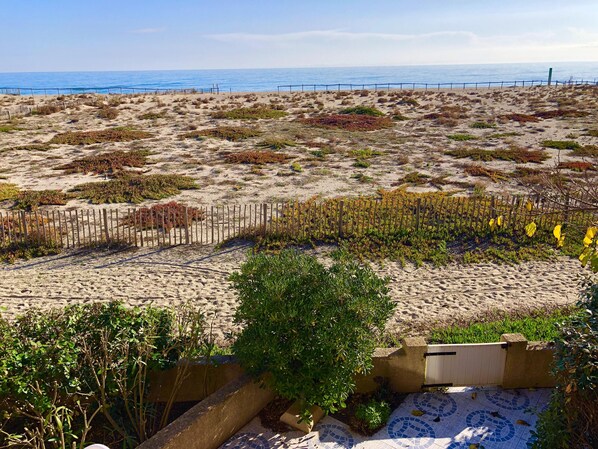 A sandy beach with sparse vegetation and a wooden fence.