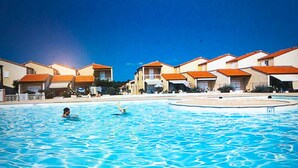 Una piscina con agua azul cristalina, rodeada de edificios con techos anaranjados y paredes blancas.