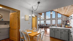 A spacious kitchen with wooden cabinets, a dining area with a wooden table and chairs, and large windows offering a view of the outdoors. - Serene cabin with gorgeous panoramic views (Sevierville)