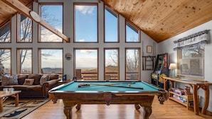 A spacious room with a pool table, a cozy seating area, and large windows offering a view of the outdoors. - Serene cabin with gorgeous panoramic views (Sevierville)