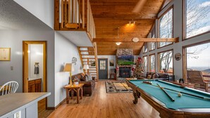 A cozy room with a pool table, wooden furniture, and large windows offering a view. - Serene cabin with gorgeous panoramic views (Sevierville)