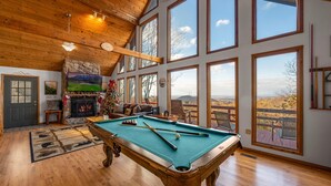 A spacious room with a pool table, a fireplace, and large windows offering a scenic view. - Serene cabin with gorgeous panoramic views (Sevierville)