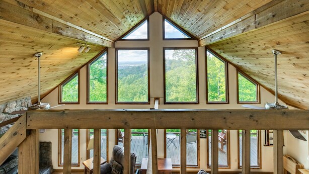 A wooden interior with a sloped ceiling, large windows, and a stone fireplace. - Serene cabin with gorgeous panoramic views (Sevierville)