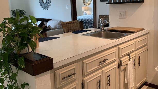 A kitchen with a central island, white cabinetry, and a backsplash. There are shelves above the sink holding glasses and cups. - Historic KMI Building - Condo, Park & Street View (Venice)