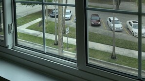 A view through a window with a grid pattern, overlooking a street with palm trees and parked cars. - Historic KMI Building - Condo, Park & Street View (Venice)