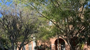 An outdoor patio with white tables and chairs, surrounded by trees and a brick building in the background. - Historic KMI Building - Condo, Park & Street View (Venice)