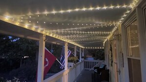 A covered porch with string lights, flags, and outdoor furniture. - PET FRIENDLY - MINUTES TO PARRIS ISLAND - BEACHES (Beaufort)