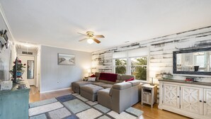 A living room with a sectional sofa, a ceiling fan, a large window, and a wooden wall. - PET FRIENDLY - MINUTES TO PARRIS ISLAND - BEACHES (Beaufort)