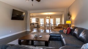 A spacious living room with a large leather sofa, a wooden coffee table, and a dining area with a chandelier.