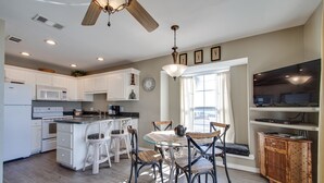 A modern kitchen with white cabinetry, a glass dining table, and a ceiling fan.