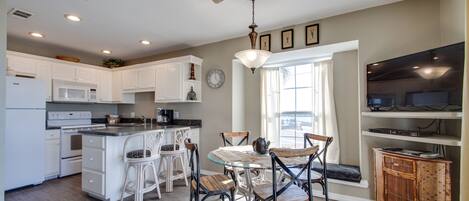 A modern kitchen with white cabinetry, a glass dining table, and a ceiling fan.