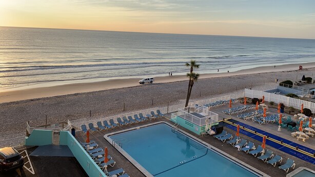 A pool area with lounge chairs and a lifeguard station, overlooking a beach with a view of the ocean.