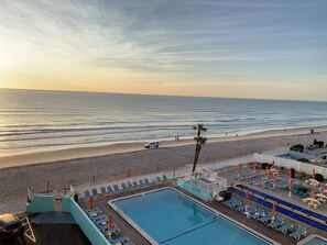 Un espace piscine avec des chaises longues et un poste de surveillance pour les sauveteurs, donnant sur une plage avec vue sur l’océan.