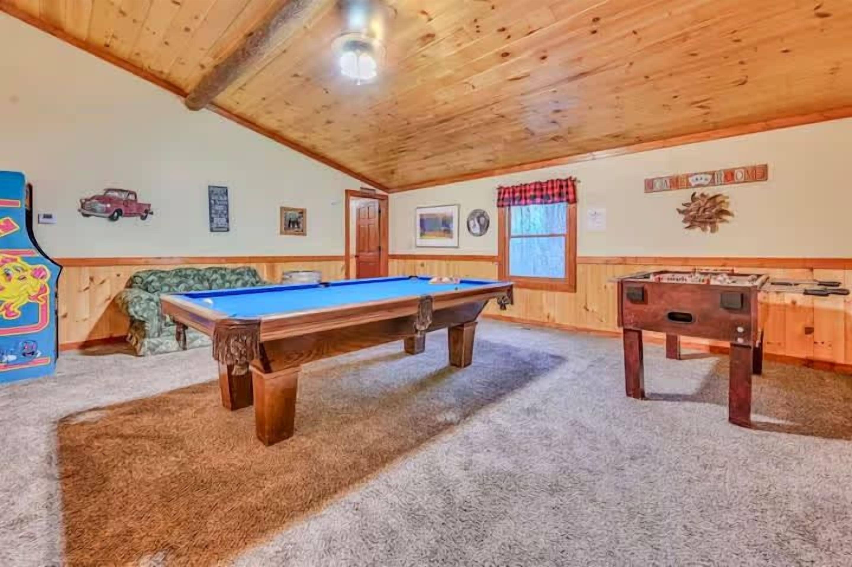 Une table de billard dans une pièce aux murs en bois et au sol recouvert d’une moquette.