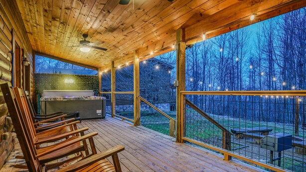 Eine Holzterrasse mit Schaukelstühlen und einem Grill, mit Blick auf ein bewaldetes Gebiet.
