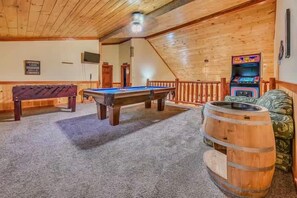 A pool table, a bar stool, and a wooden barrel in a room with wooden walls and a sloped ceiling.